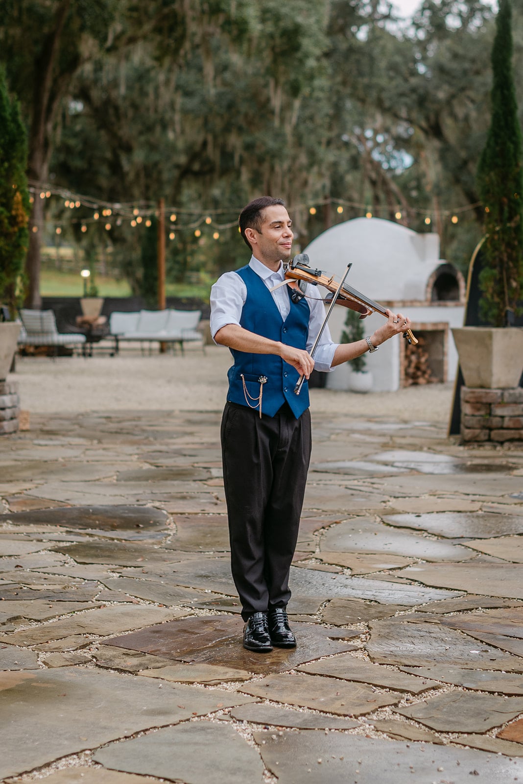 David Chirinos playing violin at an outdoor wedding venue with string lights