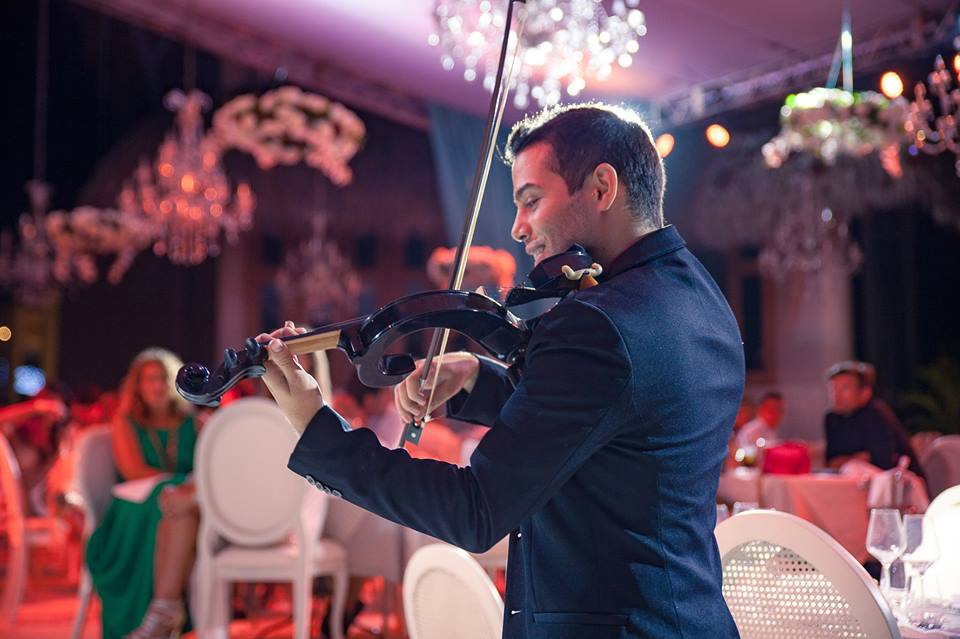 David Chirinos playing violin in a chandelier-lit ballroom at a corporate event