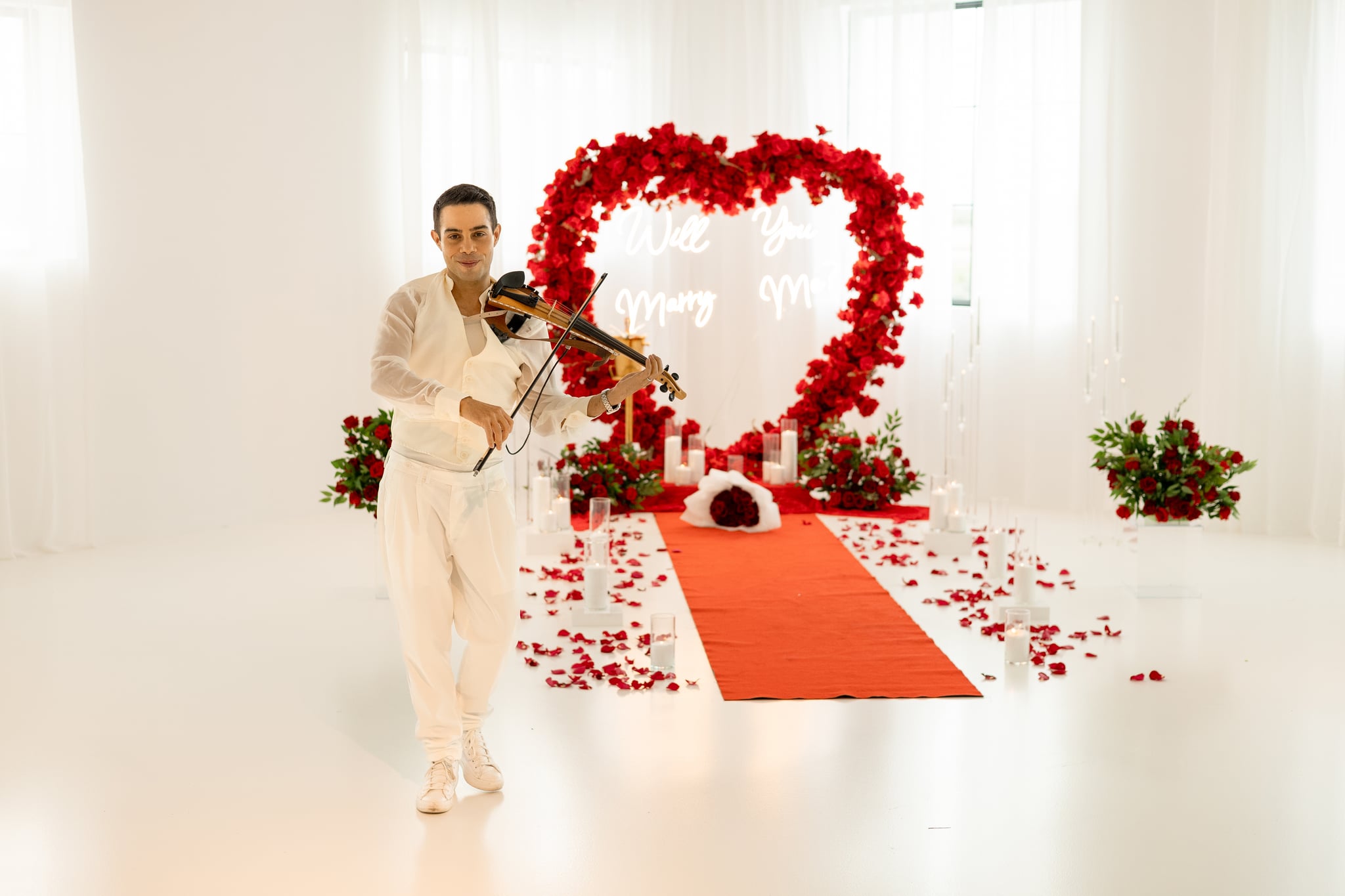 A rose heart arch with a Will You Marry Me sign and David Chirinos playing violin