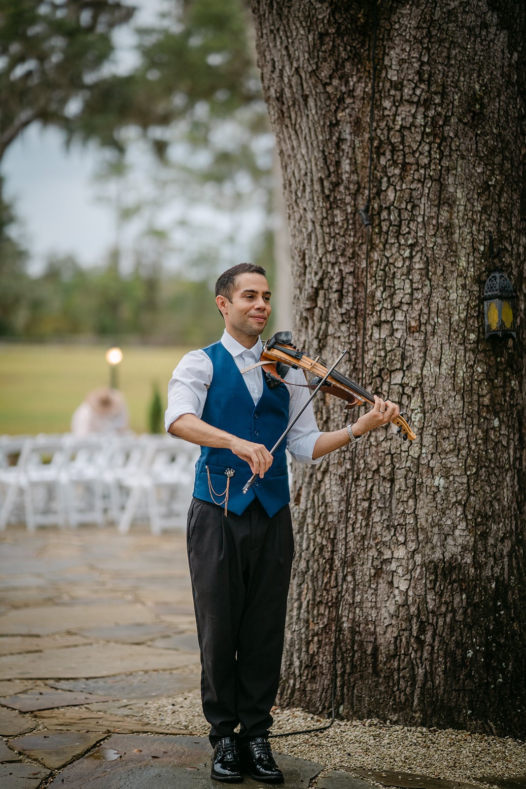 David Chirinos playing violin beside an oak at an outdoor wedding ceremony